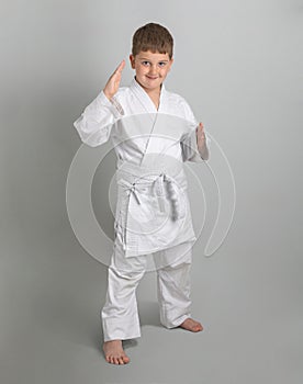 Boy in white kimono smiles and stands in combat defensive stance against gray background