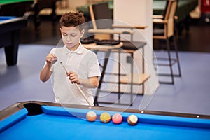 Boy in white polo-neck shirt chalks tip of cue photo