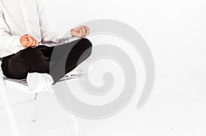 Boy in a white shirt and black trousers posing on a white background with a lotus position. The student relaxes and