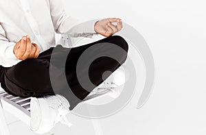 Boy in a white shirt and black trousers posing on a white background with a lotus position. The student relaxes and