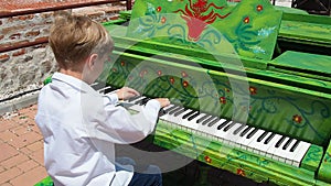 A boy in a white shirt plays the piano on the street. Child 9 years old Caucasian with blond hair. Piano painted green