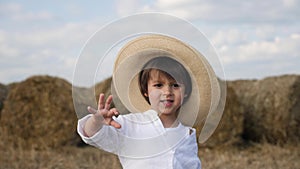 Boy in a white shirt and a straw hat is barefoot on a sloping field