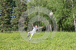 boy in white soccer uniform playing football in green summer park