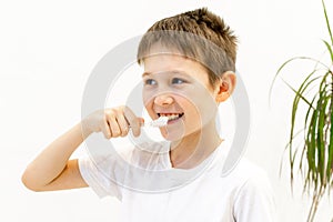 A boy in a white T-shirt is brushing his teeth in the bathroom.