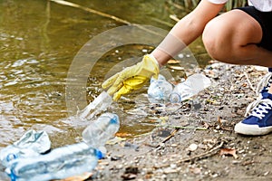 Boy in white t shirt in gloves collects garbage and plastic bottles into blue package on the beach. Young volunteer