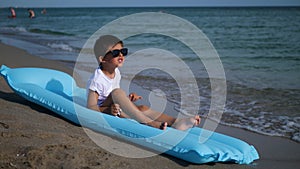 boy in a white T-shirt and striped swimming trunks lies on a sandy beach