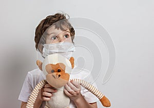 Boy in white tshirt and protective medical mask looking up with toys monkey on white background. Fight with Coronavirus epidemic