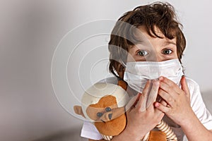 Boy in white tshirt and protective white medical mask afraid with toys monkey on white background. Fight with Coronavirus epidemic