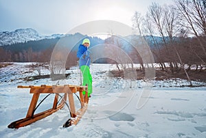 Boy in winter outfit pull wooden sledge uphill turning back