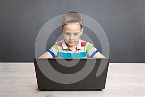 Boy works on a laptop computer and a desk. Concept of using computers for gaming and learning. Front view