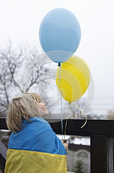 boy wrapped in a Ukrainian flag with yellow and blue balloons. Patriotic concept