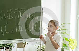 Boy writing abc letters on the green chalkboard