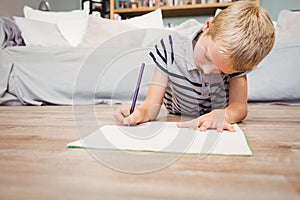 Boy writing in book while lying on hardwood floor at home