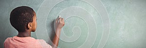 Boy writing with chalk on greenboard in school