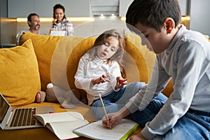 Boy writing homework exercise in notebook with sister