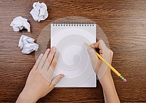 Boy writing in notepad and crumpled sheets around.