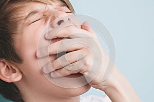 Boy yawns with his eyes closed, covering his mouth with his palm