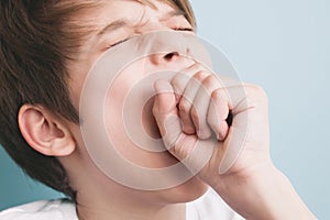 Boy yawns wide with his eyes closed, covering his mouth with his fist