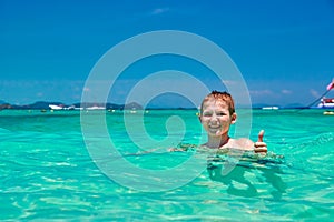 Boy 10 years old bathing in turquoise water tropical sea Child smiling while showing thumb up. Seascape with bright sky and sea