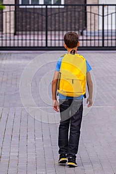 Boy with yellow backpack outdoors. Back view