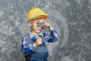 The boy in yellow hard hat holding a pipe wrench in the hands