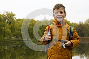 Boy in yellow jacket holding fishing rod outdoors at pond during cool autumn day