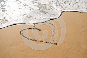 Boy in yellow rubber boots drawing heart shape on sand at the beach. School kid touching water at autumn winter sea