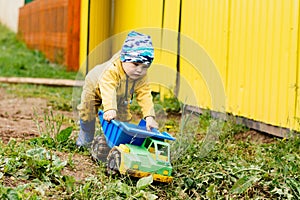 The boy in yellow suit playing with a toy car in the dirt