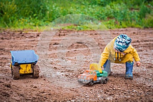 The boy in yellow suit playing with a toy car in the dirt