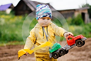 The boy in yellow suit playing with a toy car in the dirt