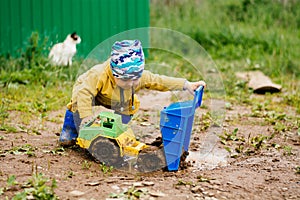 The boy in yellow suit playing with a toy car in the dirt