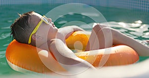 A boy in yellow sunglasses lounges in pool on inflatable ring