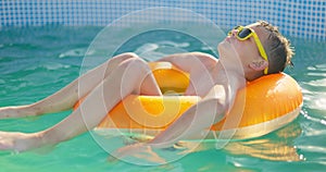 A boy in yellow sunglasses lounges in pool on inflatable ring