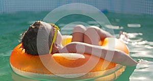 A boy in yellow sunglasses lounges in pool on inflatable ring