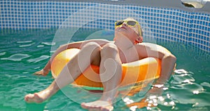 A boy in yellow sunglasses lounges in pool on inflatable ring