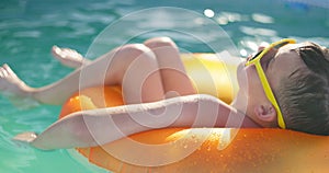 A boy in yellow sunglasses lounges in pool on inflatable ring