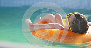 A boy in yellow sunglasses lounges in pool on inflatable ring