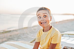 boy in yellow t-shirtsitting on bench near sea alone on beach at sunset. Happy family travel. Summer vacation with child