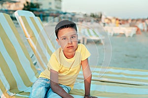 boy in yellow t-shirtsitting on bench near sea alone on beach at sunset. Happy family travel. Summer vacation with child