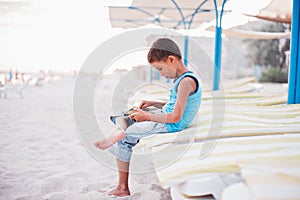 boy in yellow t-shirtsitting on bench near sea alone on beach at sunset. Happy family travel. Summer vacation with child