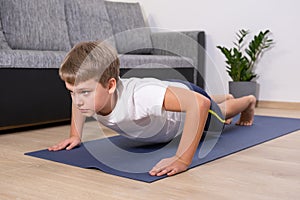 Boy on yoga mat at home holding plank pose. Child physical activity on quarantine Healhty lifestyle active leisure