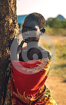 BOYA TRIBE, SOUTH SUDAN - MARCH 10, 2020: Young woman in colorful garment touching lip and looking away while leaning on