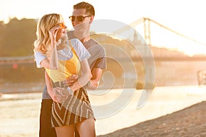 boyfriend cuddling girlfriend on river beach during sunset she