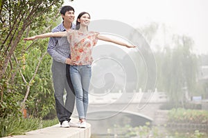 Boyfriend and Girlfriend Walking by a Canal, Arms Outstretched