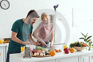 boyfriend grimacing while girlfriend cooking and talking by smartphone