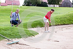 Boyfriend looking at female golfer hitting golf ball on bunker