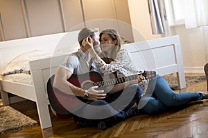 The boyfriend is playing the guitar to his girlfriend while sitting on the floor in bedroom