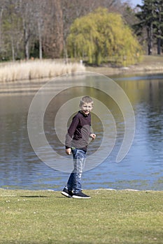 The boyl is walking along the shore of the lake in the spring