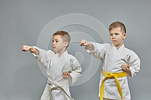 Boys athletes train hand punch on a gray background