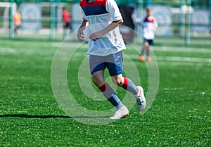 Boys at blue white sportswear run, dribble, attack on football field. Young soccer players with ball on green grass. Training